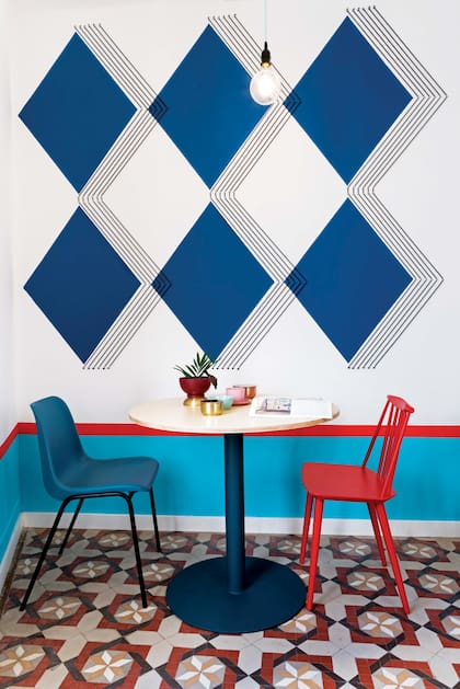 La intervención con figuras geométricas pintadas y cuerdas elásticas suma volumen y movimiento. Diseño de Masquespacio, responsable de la reforma y del interiorismo. Sillas de resina azul y roja de la serie ‘J 77’, de la firma nórdica Hay.