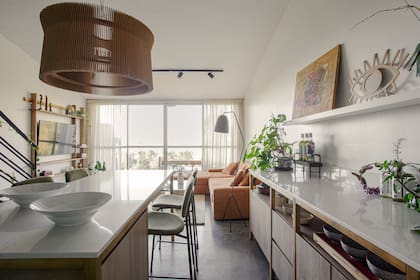 La isla con mesada de cuarzo ‘Calacatta’ y el mueble de madera maciza con frente de melamina ‘Kendal’ (Egger) convirtieron el espacio de comedor en una gran cocina abierta.