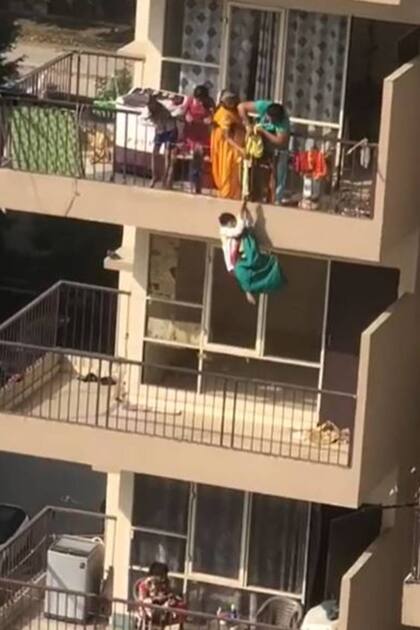 La madre y la abuela del niño tiran del sari para hacerlo subir nuevamente a su balcón