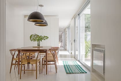 La mesa de estilo escandinavo de 1970 fue restaurada (Carpintería Álvarez) y lustrada con Bona ‘Natural’. Las sillas ‘Wishbone’ también se recuperaron: se les cambió el asiento de cuero por uno de soga. Lámparas colgantes con forma de media esfera (Lumishop). Alfombra (Seara). Florero (Tupé Home).