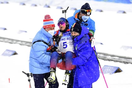 La noruega Ingrid Tandrevold es llevada en andas por compañeros de equipo, para ser atendida, luego de colapsar tras finalizar el Biatlón femenino de 10k en los Juegos Olímpicos de INvierno Beijing 2022