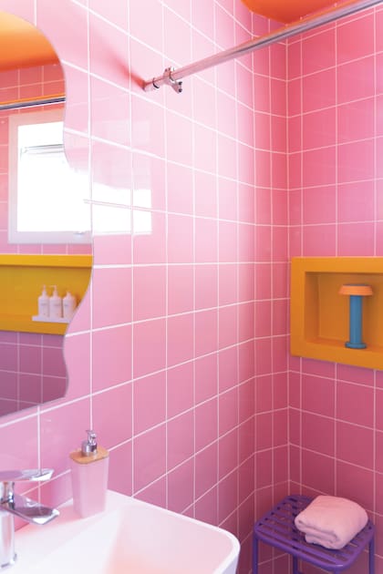 La paleta del rosa y el naranja se repite en los dos baños de la mano de los revestimientos de azulejos y cemento alisado.