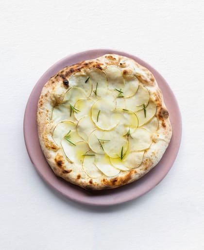 La pizza blanca de Mudrá, con crema de ajo ahumado, láminas de papa, romero fresco y aceite de oliva.
