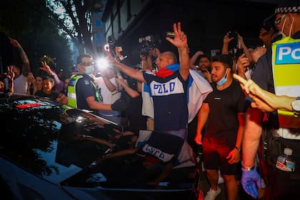 La policía intenta contener a los partidarios del serbio Novak Djokovic mientras rodean un automóvil que sale de las oficinas de su equipo legal