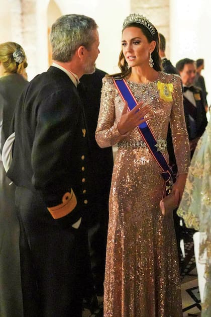 La princesa de Gales complementó su vestido de Jenny Packham con la tiara Lover’s Knot que en 1913 María de Teck,tatarabuela de William, encargó a la joyería Garrard. Le sumó la banda de la Real Orden Victoriana que le entregó Isabel II en 2017, la estrella de la Orden Real Victoriana y un broche art déco de diamantes.