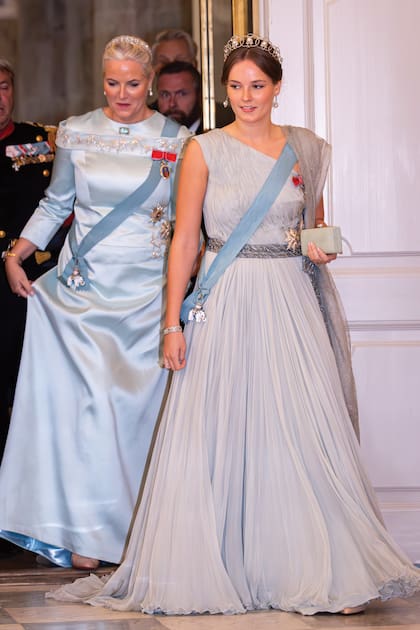 La princesa Ingrid de Noruega con un bello diseño en gasa, sin mangas y ceñido a la cintura por un cinturón de pedrería de Emilio Pucci, que complementó con zapatos Louboutin y una diadema con círculos de diamantes engastados en platino y botones de diamantes y perlas, la misma que lució para su 18 cumpleaños. Detrás, su madre, Mette-Marit, con un vestido de manga larga del noruego Peter Dundas, con cuello cerrado y detalles de pedrería en el pecho, la espalda y los hombros. La mujer del príncipe real Haakon eligió la tiara de platino, oro blanco y diamantes que había usado para su boda.