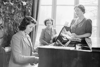 La princesa Isabel toca el piano mientras su madre, la reina Isabel, y la princesa Margarita observan en el Royal Lodge del Castillo de Windsor, Inglaterra, el 11 de abril de 1942. (Photo by Studio Lisa/Getty Images)