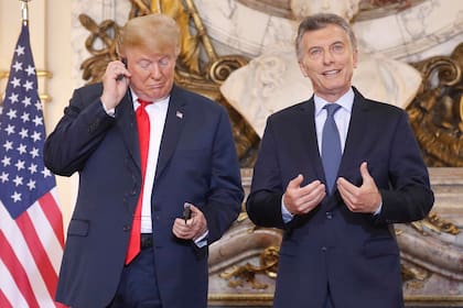Donald Trump ajustando el dispositivo de traducción de audio mientras Mauricio Macri le da la bienvenida