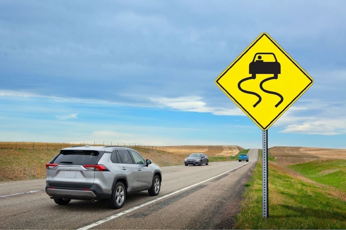 La señal preventiva con un automóvil y líneas onduladas sobre un rombo amarillo, conocida en Estados Unidos como Slippery When Wet, advierte que el pavimento puede volverse resbaladizo