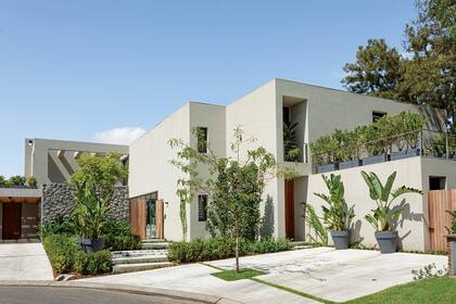 La vista exterior muestra la fachada con revestimiento pétreo ‘Raya 2’ (Tarquini) y el balcón con barandas de acero inoxidable con tensores (DMI Metalúrgica). La casa cuenta con paneles fotovoltaicos y una bomba de calor con geotermia que le dan máxima eficiencia energética.