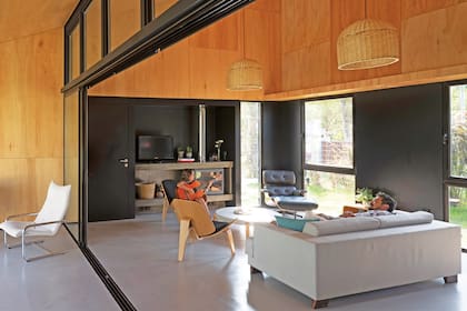La zona del living está dispuesta en torno al hogar a leña modelo ‘Liseo L71’ (Inotal) con una mesa ratona redonda, sillones individuales ‘Shell Chair CH07’, del diseñador Hans Wegner, y la clásica poltrona Eames de cuero y madera.