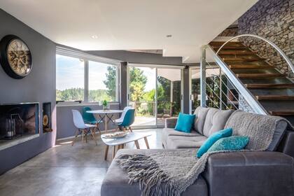 Las aberturas de aluminio con vidrios DVH garantizan el ahorro de energía. La escalera lleva al cuarto principal. Consolas, sillones y juego de mesa y sillas (Diseño Hábitat). El hogar a leña está justo arriba de una salamandra de la planta baja.