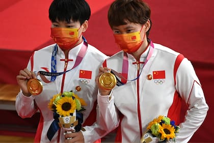 Las ciclistas chinas Bao Shanju y Zhong Tianshi con la medalla de oro en Tokio, y las insignias de Mao en los pines (Photo by Greg Baker / AFP)