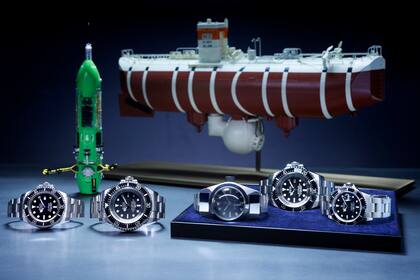 Las diferentes versiones de los relojes para bajar a la fosa de las Marianas: de izquierda a derecha, los Oyster Perpetual Rolex Deepsea (2012), Oyster Perpetual Deepsea Challenge (2022), Deep
Sea Special (1960), Rolex Deepsea Challenge (2012) y Oyster Perpetual Submariner (1986); atrás de ellos, el sumergible Deepsea Challenge y el batíscafo Trieste