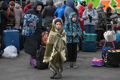 Las personas se paran con su equipaje mientras esperan para abordar los ómnibus que los transportarán más lejos en Polonia o en el extranjero desde el refugio temporal para refugiados ubicado en un antiguo centro comercial entre la frontera con Ucrania y la ciudad polaca de Przemysl, en Polonia, el 8 de marzo de 2022