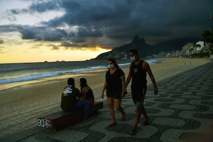 Las personas usan mascarillas como medida preventiva contra el nuevo coronavirus, mientras caminan por la playa de Ipanema en Río de Janeiro el 19 de mayo de 2020
