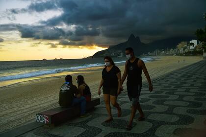 Las personas usan mascarillas como medida preventiva contra el nuevo coronavirus, mientras caminan por la playa de Ipanema en Río de Janeiro el 19 de mayo de 2020