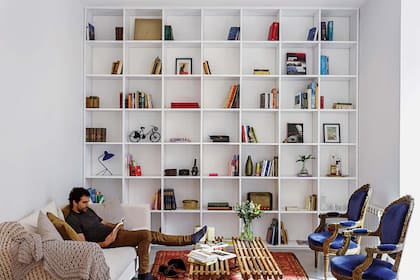 Biblioteca laqueada hecha a medida, sofá con funda de tussor (todo Estudio MMS) y mantas de hilo de algodón (Hilo Argentina), mesa lateral (Crate & Barrel), alfombra (Kasbah) y bancos en V colocados como mesas bajas (Net Muebles). Flores (Regiacasa).