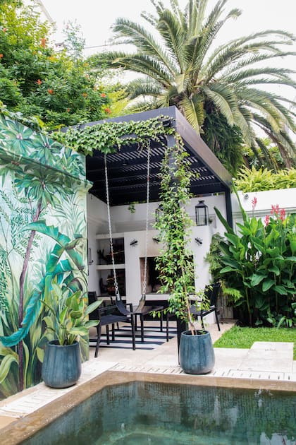 Las Strelitzia reginae plantadas en las macetas móviles se repiten en el mural, lo que aporta continuidad y armonía. Un jazmín de leche trepa por la columna de la pérgola y se funde con la ampelopsis que viene del vecino. Se gana visualmente por detrás con un gran follaje de Phoenix canariensis. Contra la medianera blanca del lateral derecho, alpinias, helechos y alocasias, que la visten densamente