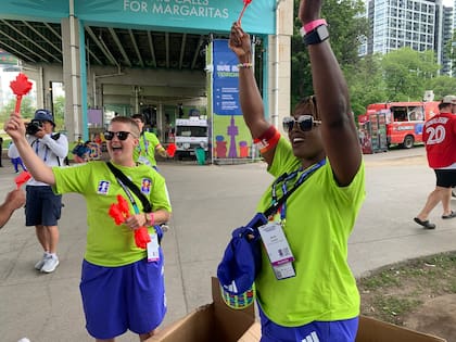 Las voluntarias Nicole Johnston (izquierda) y Mbalu Lumor (derecha) agitan aplaudidores canadienses ("Canadian clappers") antes de repartirlos a los asistentes en el FIFA Fan Festival, el miércoles 24 de junio de 2026, en Toronto. (Foto AP/Mike Householder)