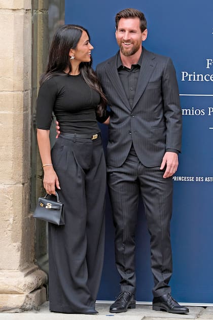 Leo Messi y su mujer –con conjunto negro de pantalón y remera tejida, stilettos y una mini Kelly de Hermès– a su llegada a Oviedo
