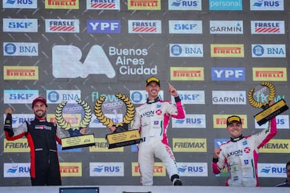 Leonel Pernía marca el N°1 con el dedo índice de la mano izquierda en el podio del autódromo Oscar y Juan Gálvez, de Buenos Aires; Julián Santero y Facundo Marques, acompañan al ganador en el estreno del calendario de TC2000