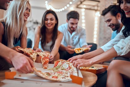 Let the party begin! Group of young people having fun together. Sitting in big light room with champagne and pizza. Celebrating holiday in big company of close friends.