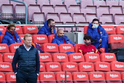 Lionel Messi se sienta en el banco mientras el entrenador del Barcelona, Ronald Koeman, se para en la línea lateral durante el partido entre Barcelona y Betis.