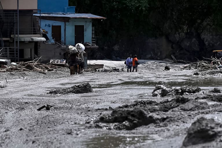 Local residents carry salvaged belongings from houses lying deluged in sludge after flash floods in the Devighat area in Nepal's Nuwakot district on August 27, 2026. Rescue teams rushed on August 27 to find more than 1,300 people missing on the Nepal-Tibet border in flash floods and landslides that killed at least 165 and swept away entire villages. (Photo by Prakash MATHEMA / AFP)