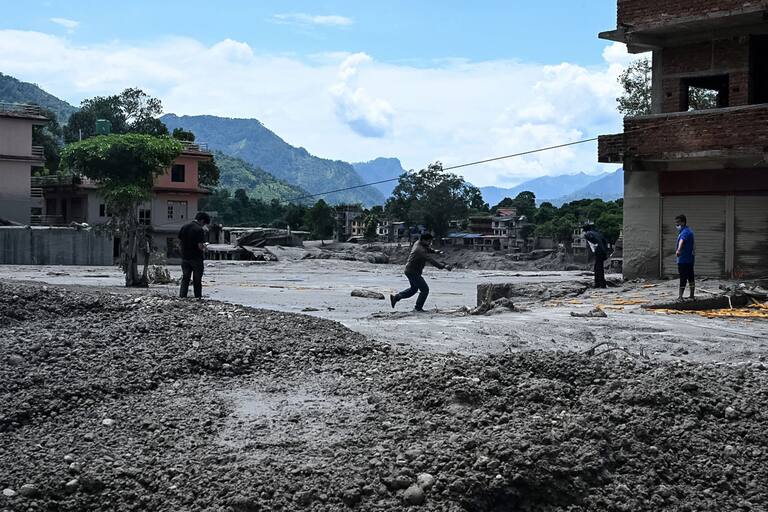 Local residents clear mud and debris from houses lying deluged in sludge after flash floods in the Devighat area in Nepal's Nuwakot district on August 27, 2026. Rescue teams rushed on August 27 to find more than 1,300 people missing on the Nepal-Tibet border in flash floods and landslides that killed at least 165 and swept away entire villages. (Photo by Prakash MATHEMA / AFP)