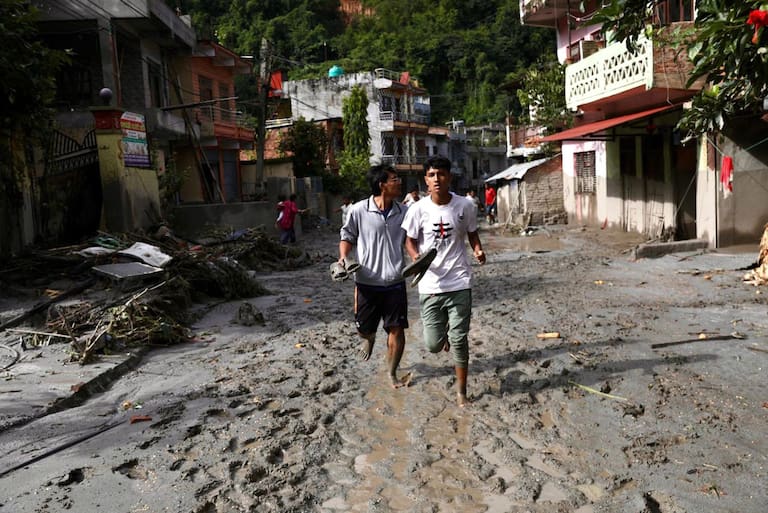 Local residents walk along a street lying deluged in sludge after flash floods near Devighat, Bidur Municipality in Nepal's Nuwakot district on August 27, 2026. Nepal's disaster agency said that 823 people remained out of contact on August 27, more than 24 hours after a deadly flood tore through the border region with Tibet. (Photo by Prabin RANABHAT / AFP)