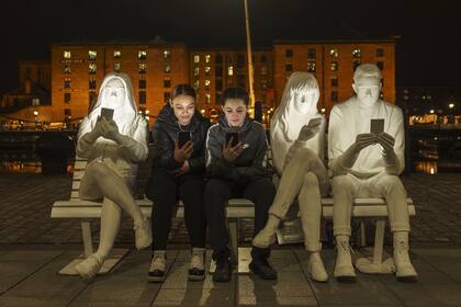 Los adolescentes posan con sus teléfonos junto a la instalación de luces 'Absorbed By Light' que se enciende antes del lanzamiento oficial del River of Light Trail anual de Liverpool el 22 de marzo de 2021.