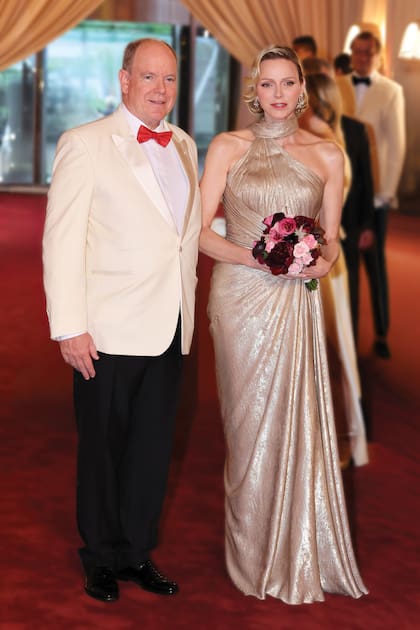 Los anfitriones de la noche: Alberto, impecable con smoking de chaqueta marfil, y Charlene, con un sofisticado vestido dorado de escote asimétrico, cuello halter, silueta fluida y capa, firmado por Elie Saab