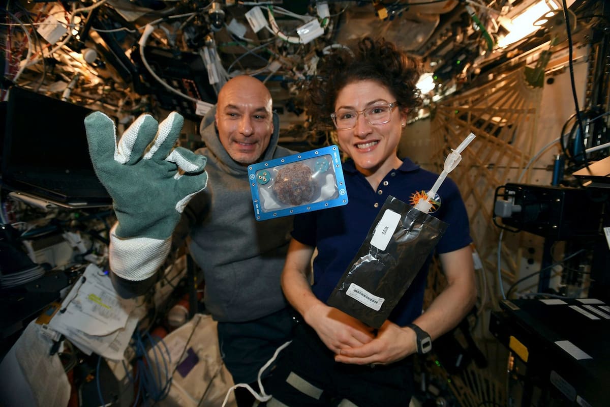 Los astronautas Luca Parmisano y Christina Koch en la Estación Espacial Internacional; en primer plano, una de las galletitas que hornearon en órbita