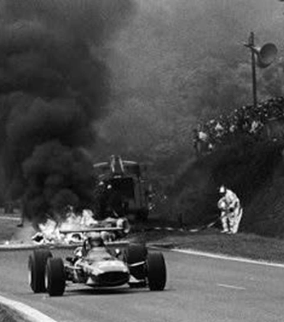 Los autos pasan por la zona del accidente, donde el auto de Jo Schlesser se consume en medio del fuego