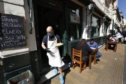 Un mozo con barbijo y guantes acerca el pedido a una mesa, en el barrio de San Telmo