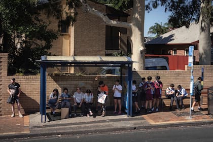 Los estudiantes revisan sus teléfonos mientras esperan el colectivo, en Sidney