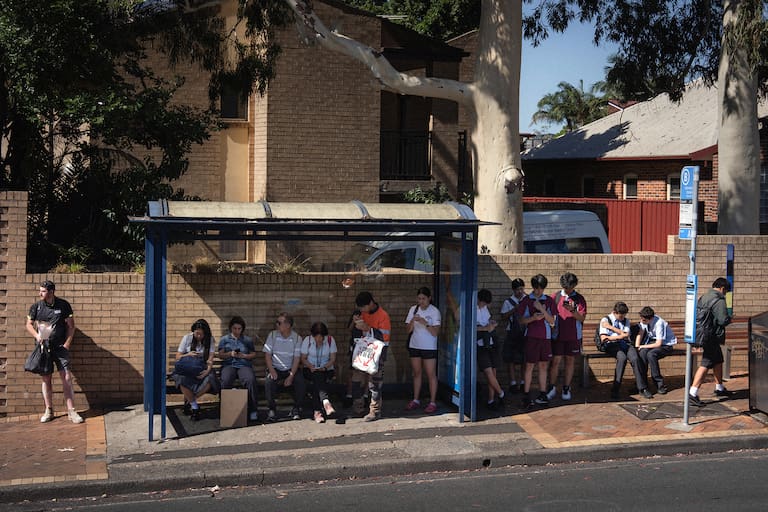 Los estudiantes revisan sus teléfonos mientras esperan el colectivo, en Sidney