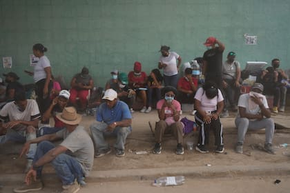 Los familiares se sientan en la acera mientras esperan a que los trabajadores retiren los escombros de los edificios derrumbados en La Guaira