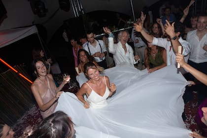 Los invitados, entre ellos Boy Olmi, sostienen la falda del vestido de Agustina, mientras ella se mueve en el centro de la ronda al compás de la música.