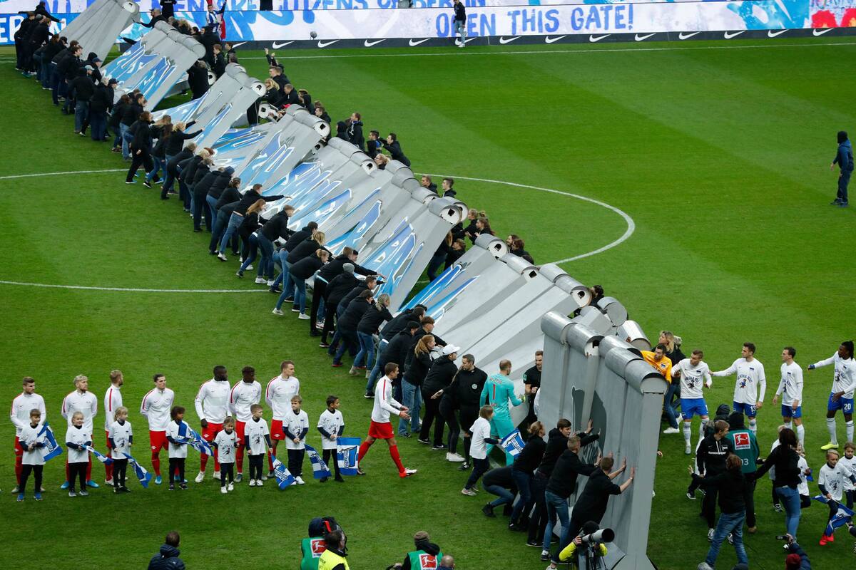 Los jugadores de Hertha y Leipzig se saludan por un improvisado agujero en una réplica del muro de Berlín, a 30 años de su caída.