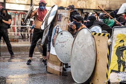 Los manifestantes se protegen de los gases lacrimógenos y los balines que disparan los carabineros