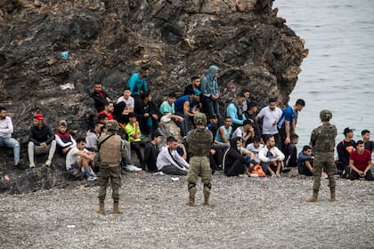 Los migrantes marroquíes se escabullen a través de una valla en la ciudad norteña de Fnideq en un intento de cruzar la frontera de Marruecos al enclave español de Ceuta en el norte de África el 18 de mayo de 2021. - Al menos 5.000 migrantes, una afluencia sin precedentes en un momento de alta tensión entre Madrid y Rabat entraron a Ceuta el 17 de mayo, un récord para un solo día, dijeron las autoridades españolas. Llegaron al enclave nadando o caminando durante la marea baja desde las playas a pocos kilómetros al sur, algunas con anillas inflables para nadar y botes de goma.