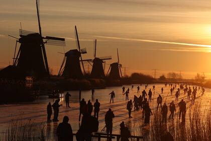 Los patinadores se deslizan sobre el hielo cerca de los molinos de viento en el pueblo de Kinderdijk en Holanda el 14 de febrero de 2021