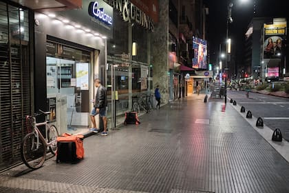 En medio de avenida Corrientes vacía un repartidos espera un pedido en la puerta de un local de comidas