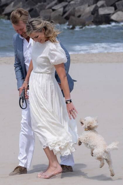 Los Reyes disfrutan de una caminata por la playa. Máxima, con un conjunto de lino de la diseñadora Tory Burch compuesto por top de manga corta con volumen y falda bohemia que complementó con sandalias taco chino de Jimmy Choo. Guillermo Alejandro, con pantalón y camisa blancos y saco azul.