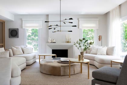 Los sofás curvos tapizados en lino son un diseño exclusivo de las interioristas Celina Azpiroz y Malena Perkins para esta casa en Nordelta, al igual que la mesa circular de cuero y las mesas de arrime. Lámpara colgante (Estudio Molé).