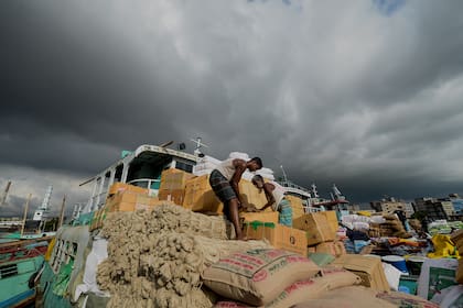 Los trabajadores cargan mercancías en un barco de carga en el río Buriganga mientras las nubes de lluvia se ciernen sobre Dhaka el 9 de agosto de 2020