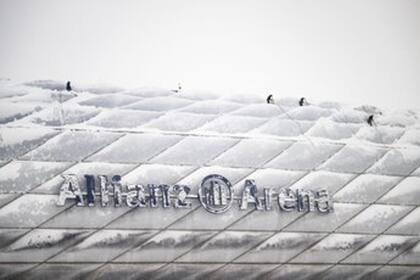 Los trabajadores del Allianz Arena "escalan" sobre el estadio para ayudar a retirar la nieve acumulada en la estructura.