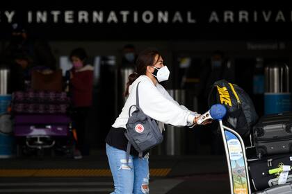 Los viajeros con mascarillas empujan carritos de equipaje en el punto de llegadas fuera de la Terminal Internacional Tom Bradley (TBIT) en el Aeropuerto Internacional de Los Ángeles (LAX)